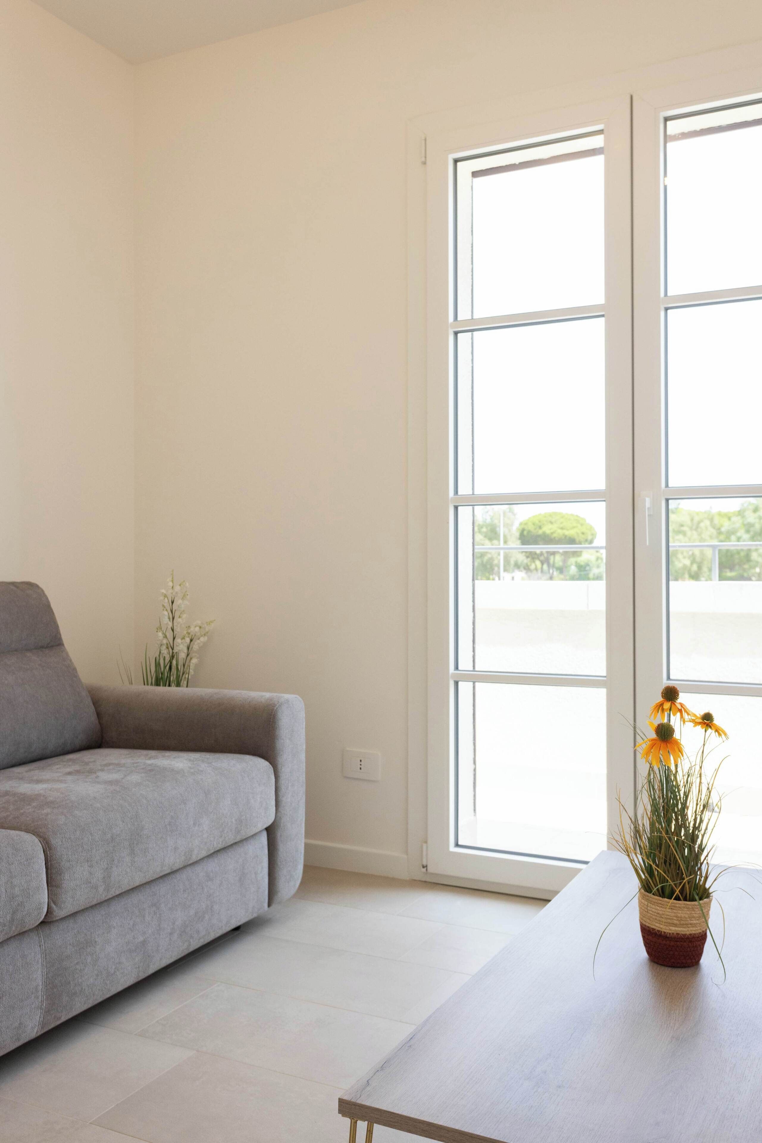 Un salón minimalista con un sofá gris, una mesa de madera y una planta en maceta con flores amarillas.