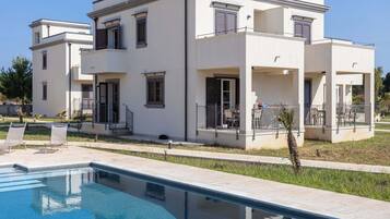 A modern two-story house with a swimming pool, outdoor furniture, and a clear blue sky.