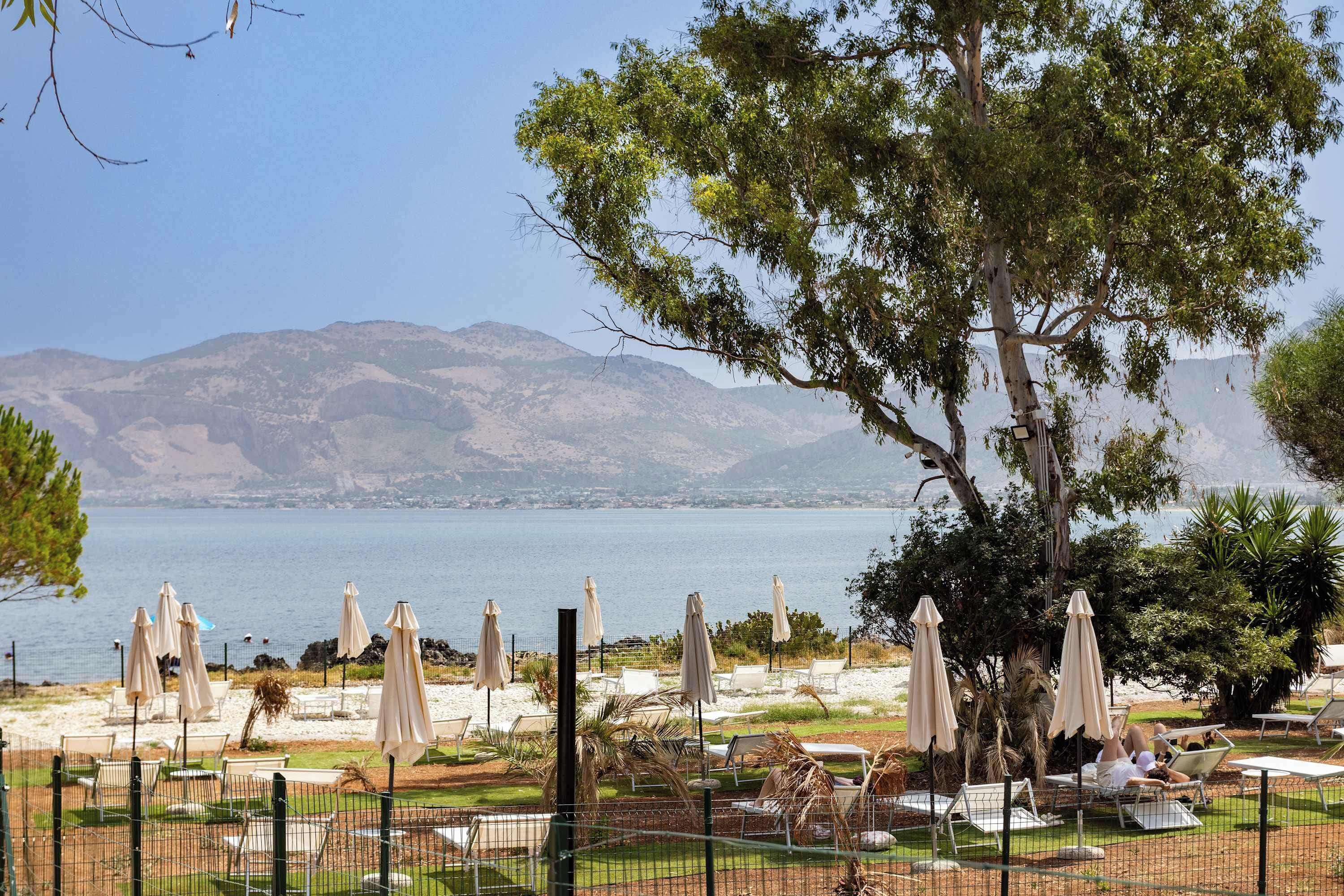 A coastal view with a seating area, umbrellas, and a view of the sea and mountains.