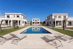 Area piscina con lettini, piscina cristallina blu e edifici moderni con balconi.