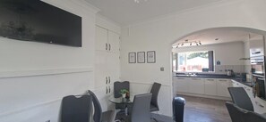 A modern kitchen with white cabinets, a dining area with a glass table, and a large window providing a view of the outdoors.