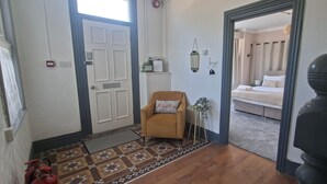 Een hotelentree met een getextureerd vloerkleed, een bruine fauteuil, een bed met hemelbed en een spiegel aan de muur.