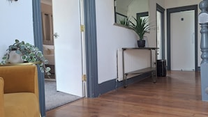 Een hal met houten vloer, een radiator, een plant in pot, een bank en een trap.