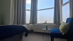 Een kamer met twee bedden, een stoel met kussen, een kleine tafel en een raam met gordijnen.