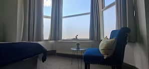 A room with two beds, a chair with a pillow, a small table, and a window with curtains. - Contractors paradise in Peterborough -sleeps 14 (Peterborough)