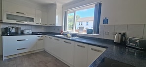 A modern kitchen with white cabinets, a black countertop, and a window with a view of a house.