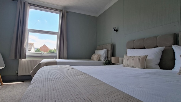 Een hotelkamer met twee bedden, een radiator, een raam met gordijnen en een stoel.