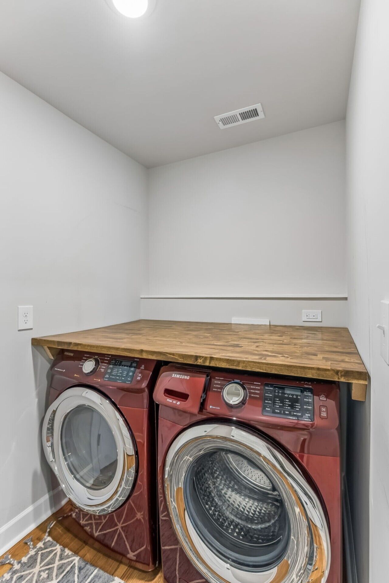 A laundry room with two front-loading washing machines and a wooden countertop.