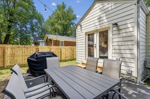 A backyard with a wooden deck, a barbecue grill, and a dining table with chairs.