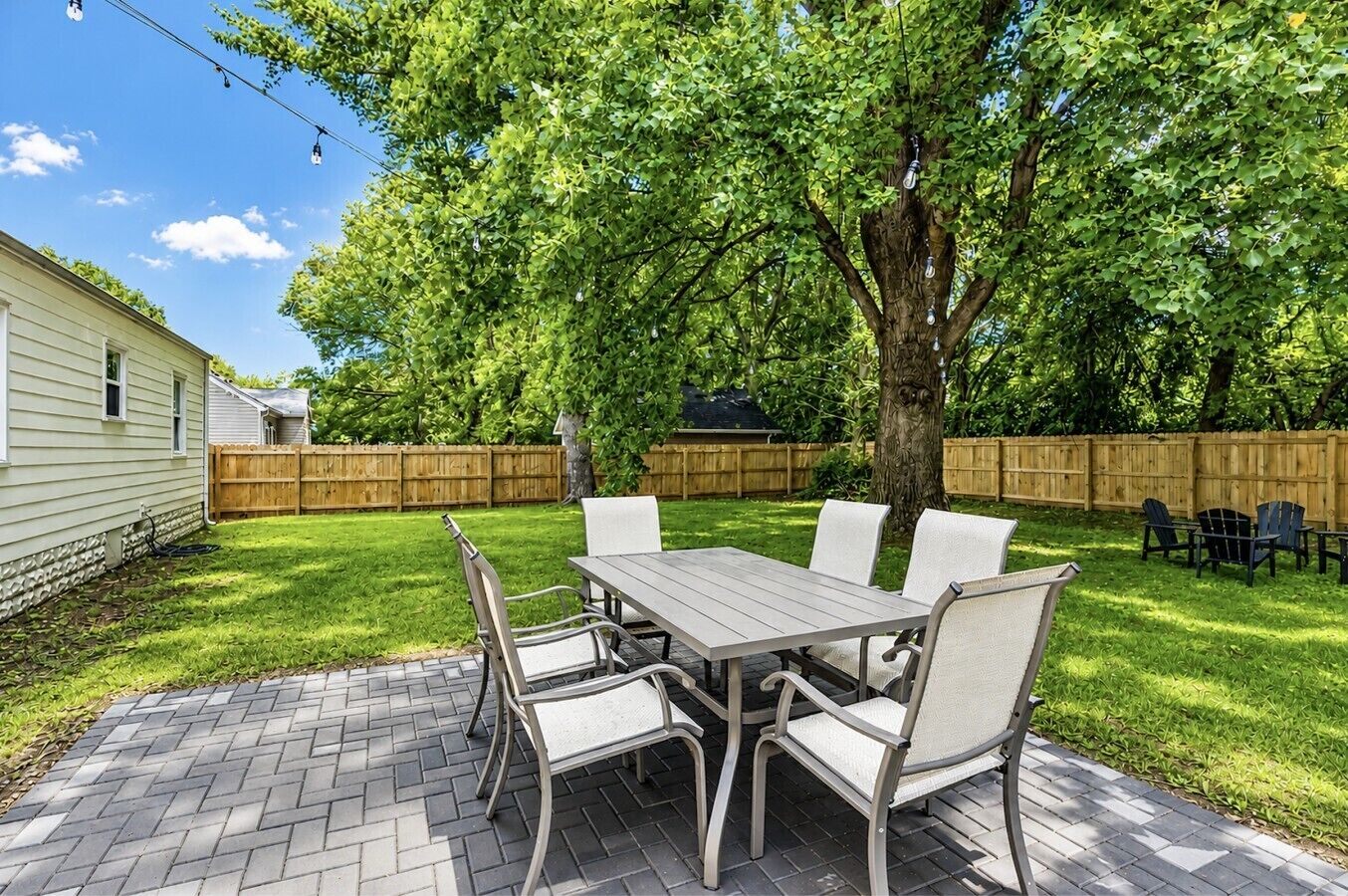 A patio with a table and chairs, surrounded by a wooden fence and a tree.