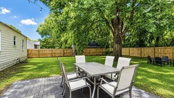 A patio with a table and chairs, surrounded by a wooden fence and a tree.