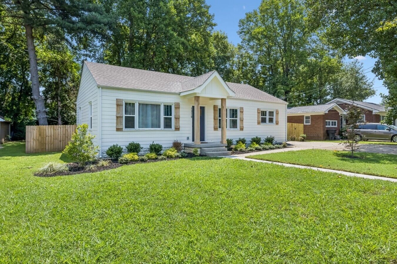 A single-story house with a front porch, a small front yard, and a wooden fence.
