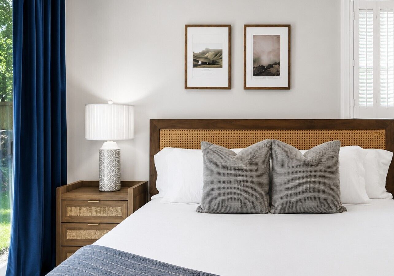 Un lit bien fait, avec deux oreillers, une lampe de chevet et deux tableaux encadrés accrochés au mur.