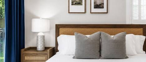 Una cama bien hecha con dos almohadas, una lámpara de noche y dos cuadros en la pared.