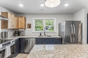 A modern kitchen with granite countertops, stainless steel appliances, and a window with blinds.