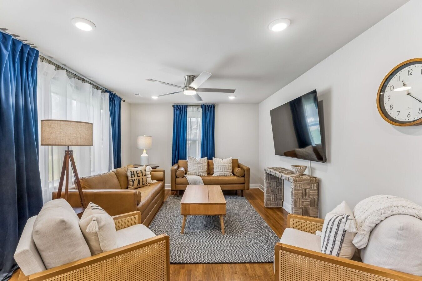 Un salon moderne avec un canapé, des fauteuils, une table basse, un téléviseur et une horloge au mur.