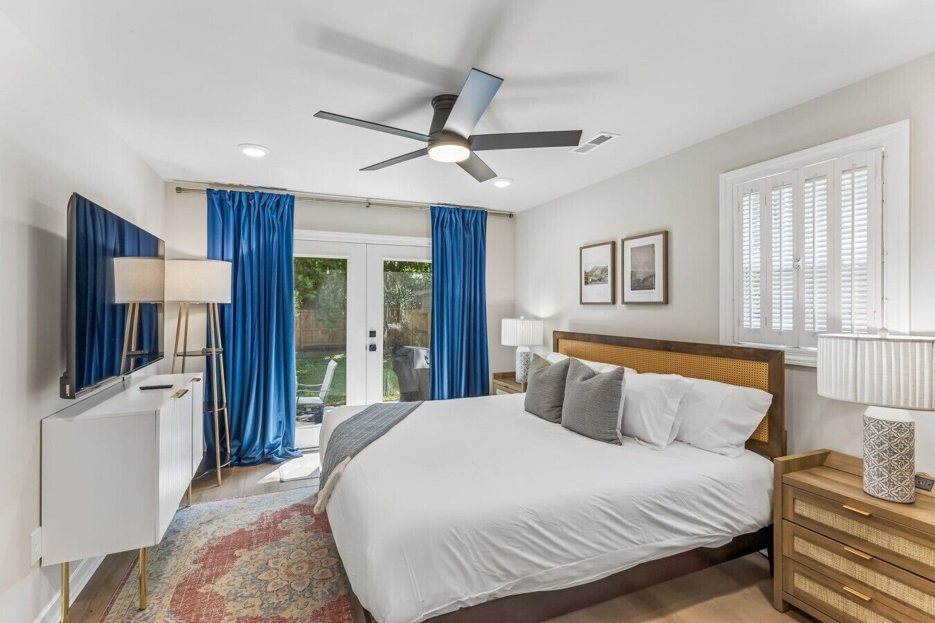 A bedroom with a bed, bedside tables, a ceiling fan, and a view of the outdoors.