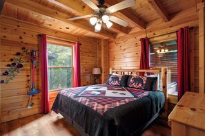 Ein Schlafzimmer einer Holzhütte mit einem Bett, einem Deckenventilator und einem Fenster mit Vorhängen.