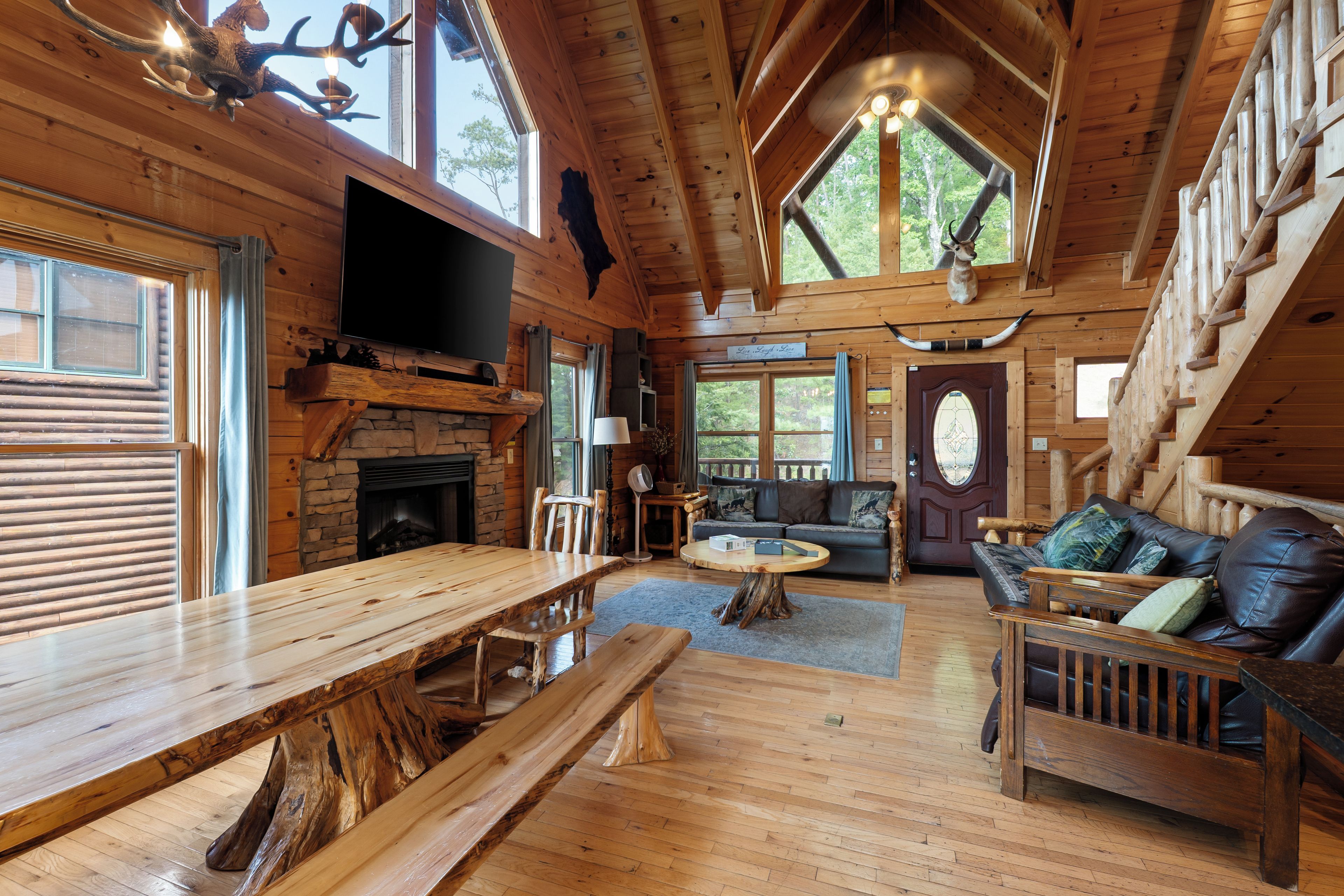A log cabin interior with a stone fireplace, wooden dining table, and a cozy seating area with a sofa and chairs.