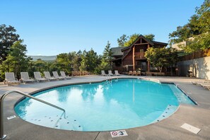 Ein Schwimmbecken mit Liegestühlen und ein Holzgebäude im Hintergrund.
