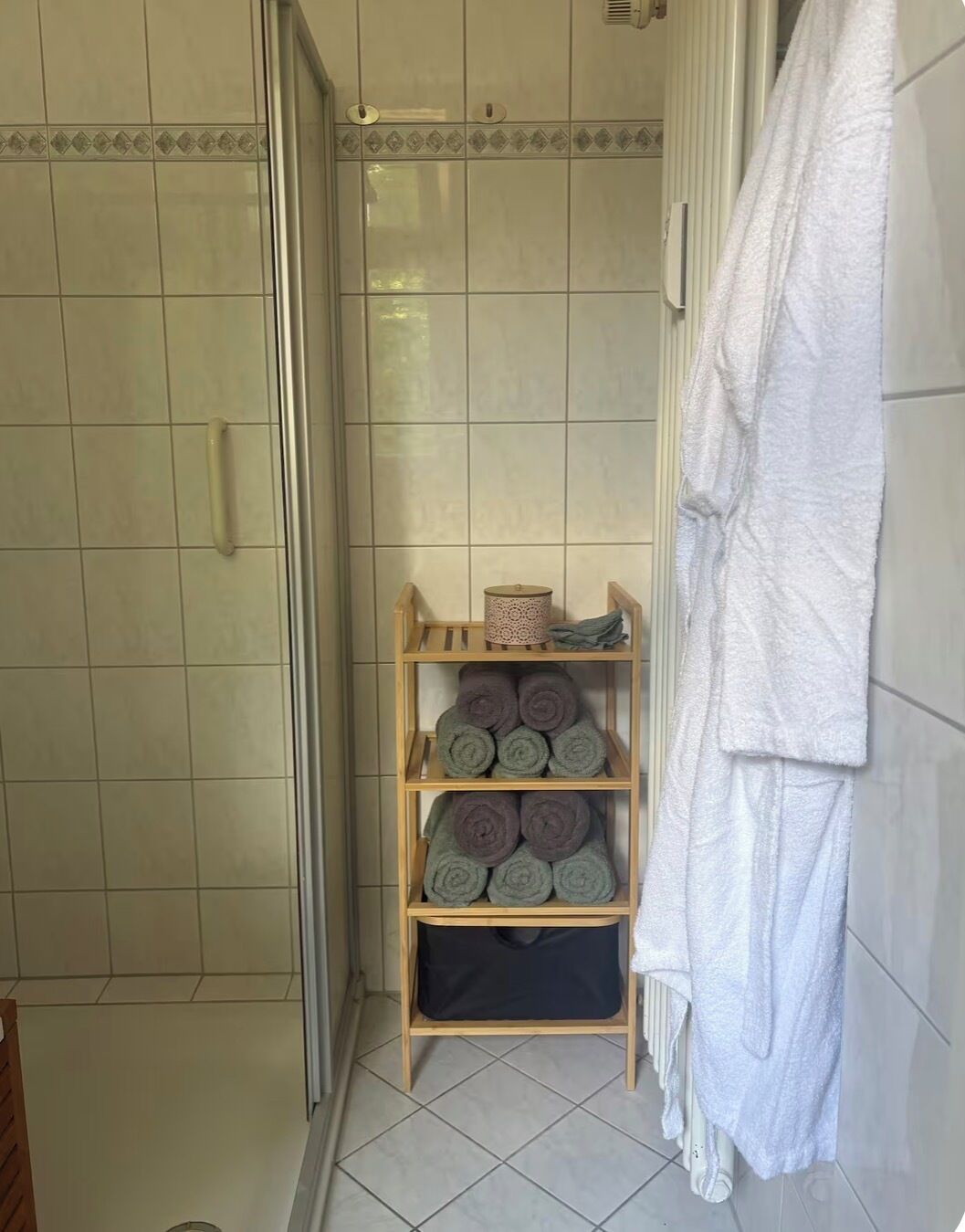 Ein Badezimmer mit Duschbereich, einem Handtuchhalter und einer Ablage für gerollte Handtücher.