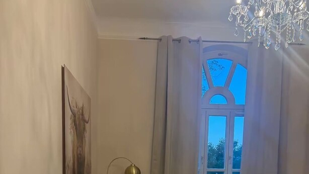Ett rum med en säng, en soffa, ett matbord med stolar, en lampa och ett fönster med gardiner.