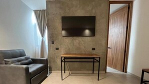A living room with a sofa, a table, a TV mounted on a textured wall, and a door. - Casa Valentina (Aguascalientes)