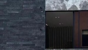 A modern building facade with a dark textured wall, a window with vertical blinds, and a metal gate. - Casa Valentina (Aguascalientes)