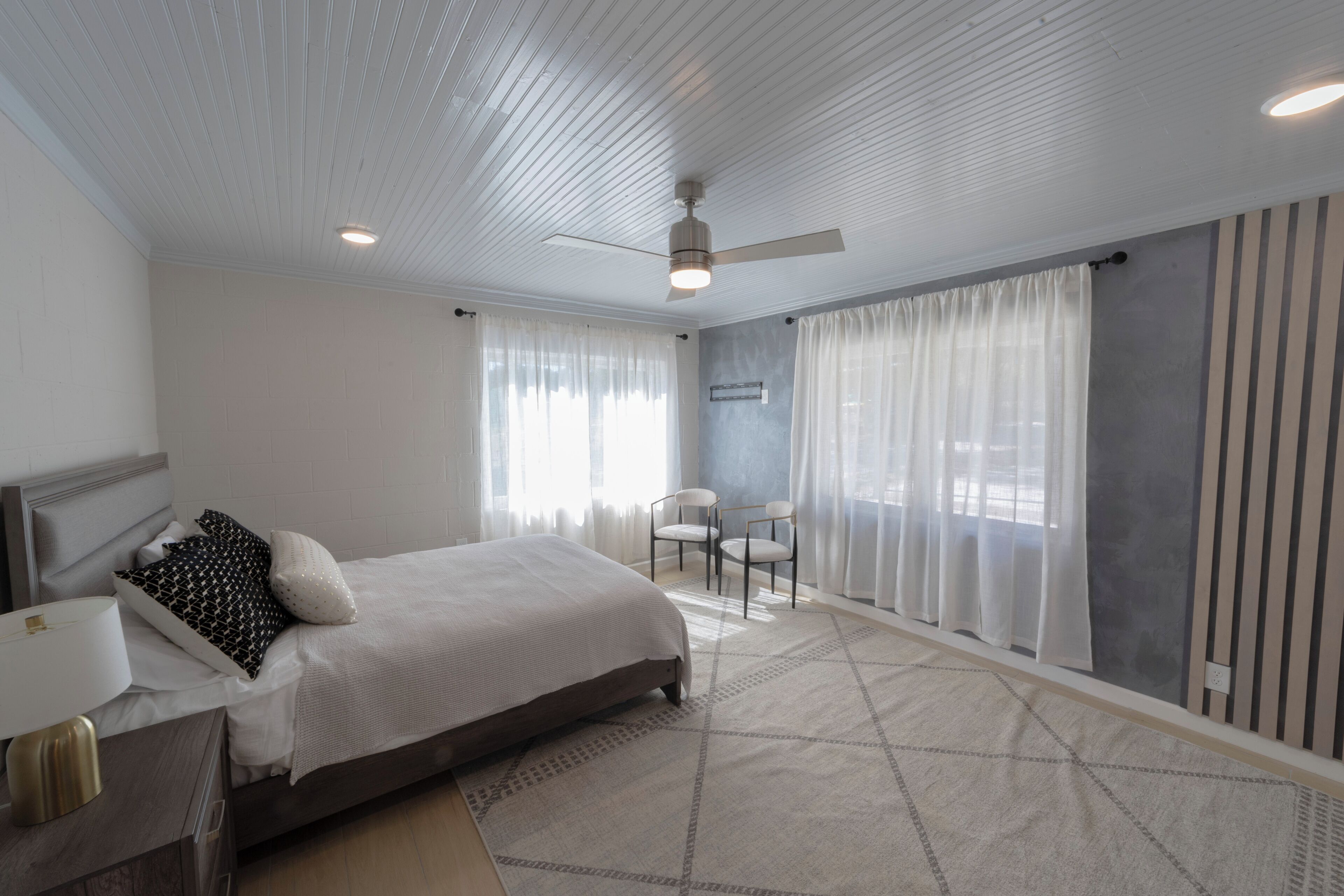Une chambre à coucher avec un lit, un bureau, une chaise et un ventilateur de plafond.