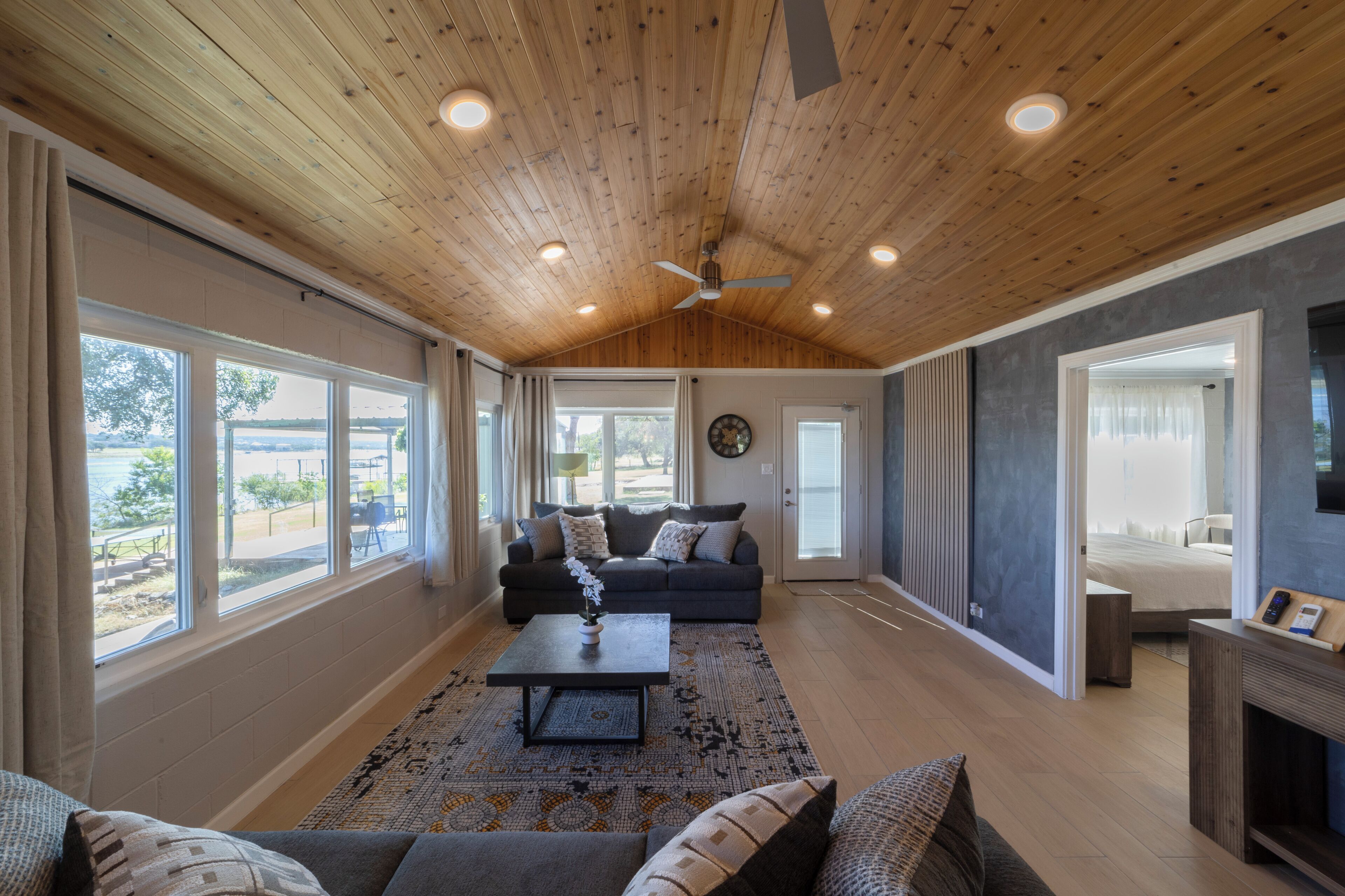 A spacious living room with a wooden ceiling, large windows, a sofa set, and a coffee table.