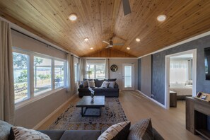 A spacious living room with a wooden ceiling, large windows, a sofa set, and a coffee table.