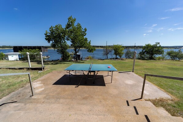 A ping pong table set up on a concrete surface with a view of a lake and trees in the background.