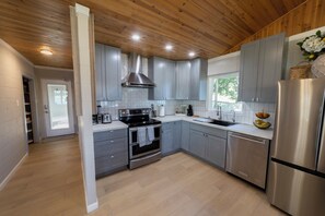 A modern kitchen with stainless steel appliances, grey cabinetry, and a wooden ceiling.
