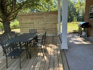 An outdoor patio with a wooden deck, a metal table and chairs, a white column, and a barbecue grill.