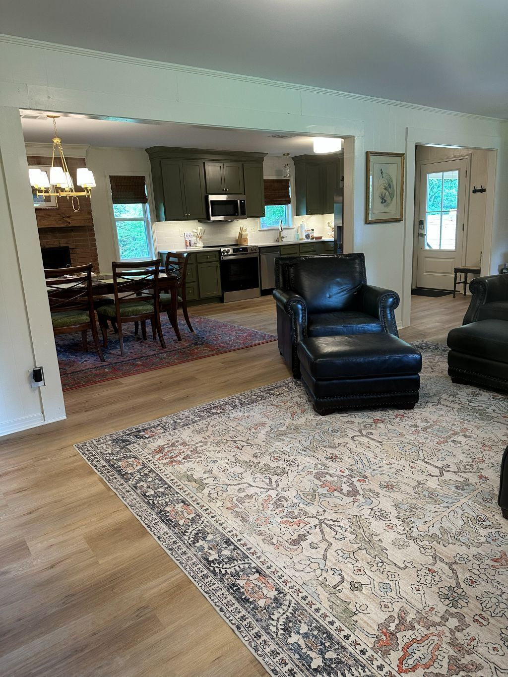 A spacious living room with a large black leather sofa, a dining area with wooden chairs, and a kitchen in the background.