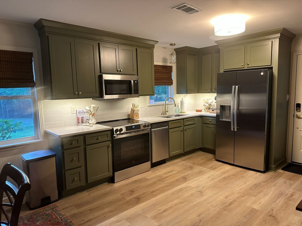 A kitchen with green cabinets, stainless steel appliances, and a window with a view.