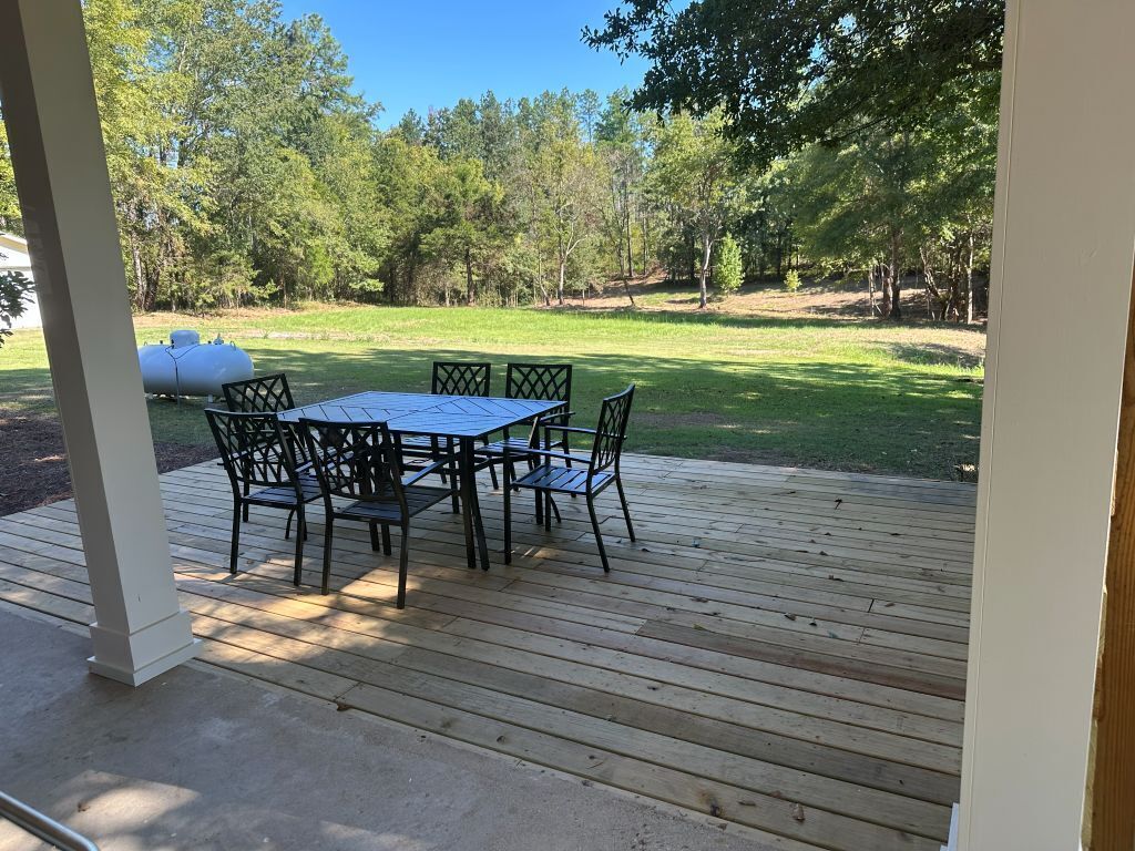 Une terrasse extérieure couverte, dotée d’une table et de chaises, entourée d’une pelouse et d’arbres.