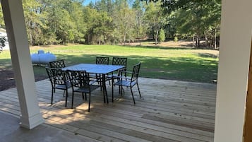 Une terrasse extérieure couverte, dotée d’une table et de chaises, entourée d’une pelouse et d’arbres.