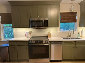 A kitchen with green cabinets, a stainless steel microwave, a stove, and a dishwasher.