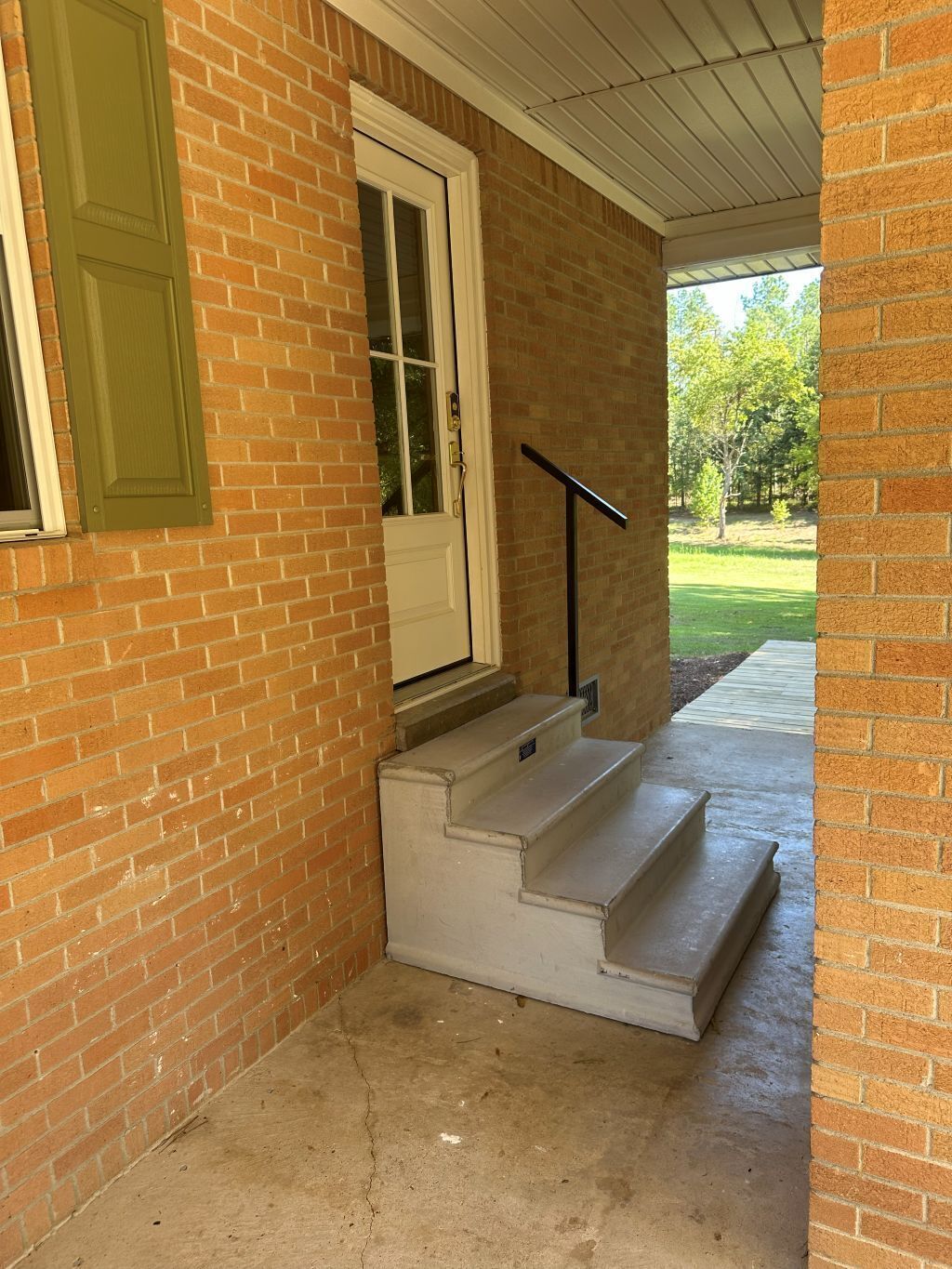 A brick exterior with a white door and green shutters, a concrete staircase, and a metal handrail.