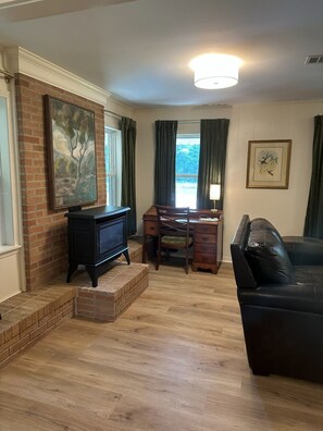 A living room with a fireplace, a wooden desk, a leather sofa, and a large window with curtains. - NEW!!!  Freshly renovated 3-bed/2-bath cottage close to Sardis Lake and Ole Miss (Sardis)