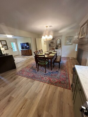 A spacious living room with a dining area, a television, and a chandelier.
