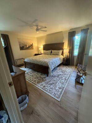 A bedroom with a bed, a ceiling fan, a nightstand, a lamp, a window with curtains, and a rug.