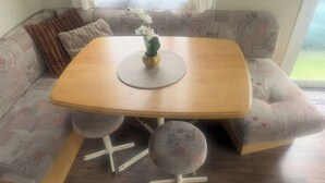 Un rincón con asientos, una mesa de madera, dos sillas, una pequeña planta en maceta y cojines estampados.