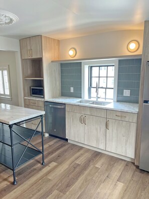 Een moderne keuken met houten kastjes, een roestvrijstalen vaatwasser en een marmeren aanrecht.
