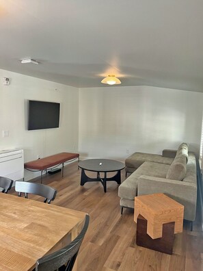 A modern living room with a flat-screen TV, a round coffee table, a sofa, a wooden dining table, and a bench.