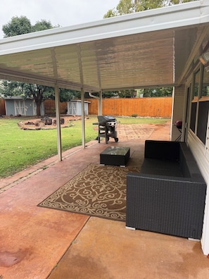 Un patio cubierto con una parrilla, muebles de exterior y un tapete estampado.