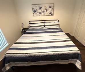 Una cama con colcha a rayas, una mesita de noche con lámpara y un cuadro colgado en la pared.