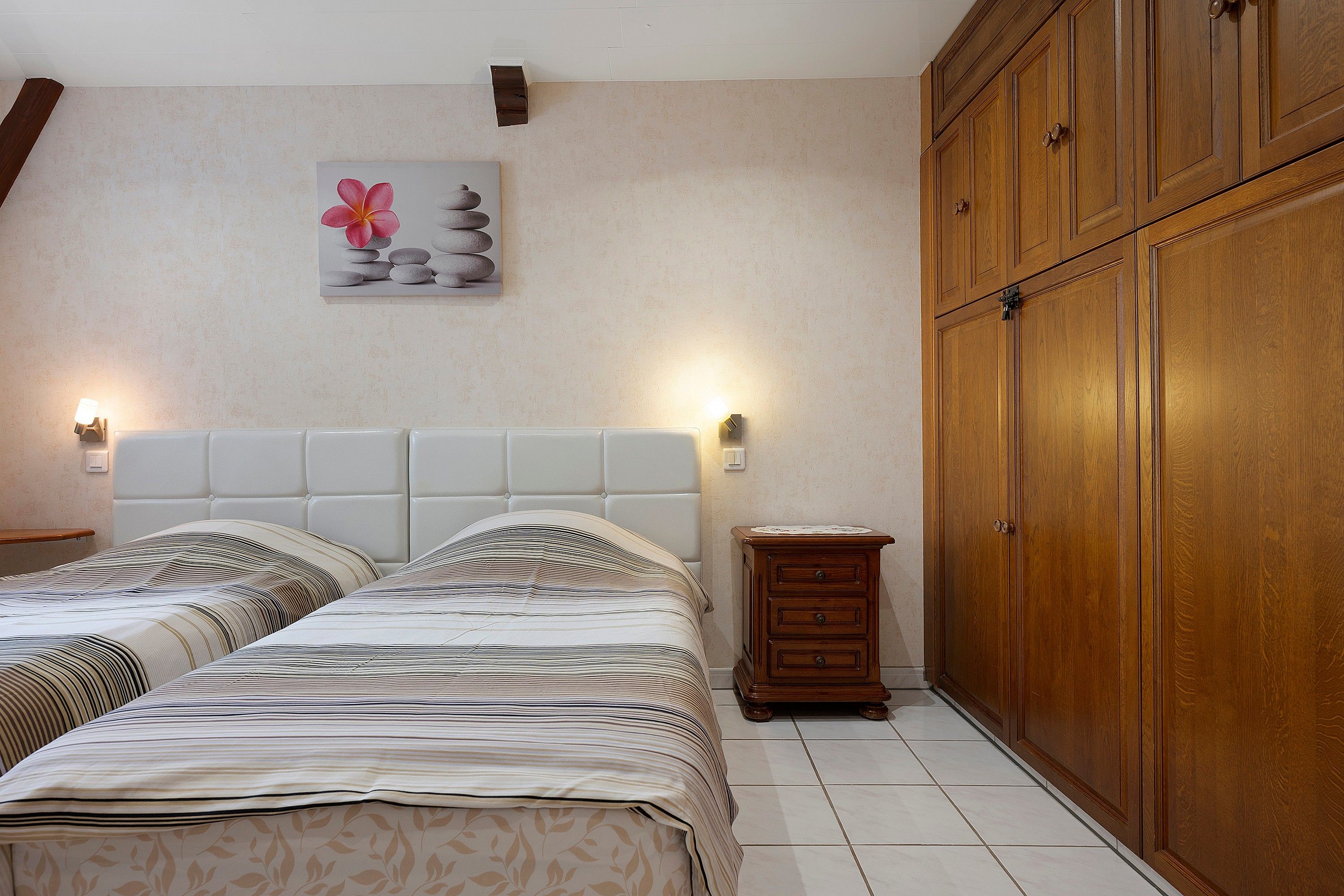 Un dormitorio con cama, mesitas de noche, aparador, armario de madera y una obra de arte en la pared.