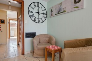 A living room with a large wall clock, a sofa, a chair, and a small table.